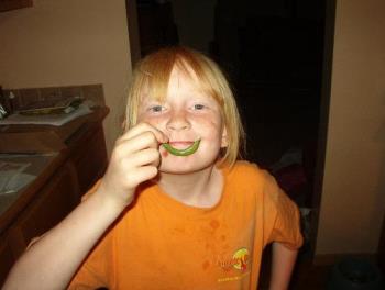 Caroline being silly showing off her 1st green bea - Caroline and I were going thru the gardens after several days of rain to see how the veges were doing and I spotted this green bean on her vine. She was all excited about it so I took her pic with it. Not very big but being the vine is only a foot tall, it's a start. 