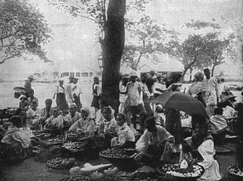 Food Market In Old Cavite - This photograph represents the native fruits, melons, etc., usually found in the markets of the various cities and towns. The stands are generally kept by women amd girls, all of whom smoke cigars and cigarettes.