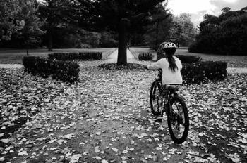 Street photography: Uncomplicated trees and happy girl safely biking with her parents watching by at dusk. Street photography: Uncomplicated trees and happy girl safely biking with her parents watching by at dusk.