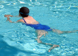 swimming -  is composed primarily of water, and thus has a very similar density to water. Roughly, 70% of the body is water; while the lungs are filled with the air, the body is slightly less dense than the surrounding water, which exerts a buoyant force on it. Thus staying afloat requires only a slight propelling of water downward relative to the body, and transverse motion only a slight propelling of water in a direction opposite to the direction of intended motion. This propelling is accomplished by using the hands and forearms as paddles, and by kicking the legs to push water away from the body (though kicking accounts for relatively little overall). Since salt water (e.g., the ocean) is denser than fresh water (e.g., most swimming pools), less effort is required to stay afloat in salt water than in fresh water.

A number of swimming styles have been developed based on the implementation of some or all of the following principles:
The torso and the legs should be kept as parallel as possible to the surface of the water. Dropped legs or a slanted torso dramatically increase drag. The hand should be extended forward of the head as much as possible. This increases the average length at the water-line, substantially increasing speed.