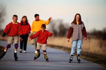 family outing - happy family bonding. Parents on walk and children playing with their roller blades. 