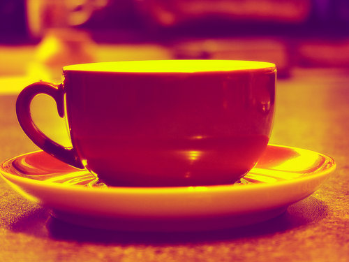 red coffee cup in coffee house - A picture of a reddish-brown or red coffee cup sitting on a counter in a coffee house. The picture has a very jazzy feel to it.  A royalty-free photo from StockXchange, www.sxc.hu