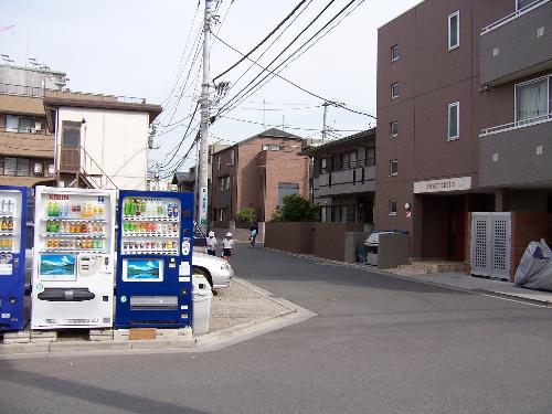 Neighborhood vending machines - A pair of boys in uniform on their way to school in a quiet suburb, with vending machines in the foreground. A train station is about six blocks from here. Vending machines with drinks are quite common but it is difficult to find them with snacks or candy.
