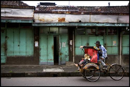 taking a ride - This picture is taken in the old part of bandung were you can see the old dutch architecture. Even if theoraticly the pedicabs are banned for the big streets they are still widely used and they often bend the rules. In indonesia the pedicabs are named becak and i was told they have been in use for over 40 years(more then that for sure). This particular on model of rickshaw is the one who won the public favor, it gradually replaced the other smaller models and is now found all over java. Riding in a becak is a very nice experiance, especially at dusk in small backlane streets.  Nowadays becaks are mainly used by housewifes coming home from the market, by small childrens going to school or by people lazy to walk from the main road to theyre house located in small alleys or housing complexes, the weather is very hot in the day time. No co2 emmissions.....