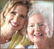 Mother and Daughter - An elderly woman with gray hair sitting with another woman with their heads together smiling. They seem happy and content. This is a photo of an aging mother and a 40 something daughter.