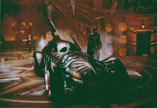 The Batmobile-Batman's ride. - The Batmobile with The Dark Knight himself. A still from the movie Batman Forever. We can also see Alfred behind the Batmobile near the silver Bat-Symbol on the wall of the Bat-Cave.
