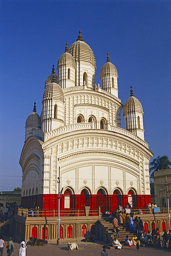Kali temple of Dakshineswar - In the year 1847, the wealthy widow Rani Rasmani prepared to go upon a long pilgrimage to the sacred city of Banaras to express her devotions to the Divine Mother. In those days there was no railway line between Calcutta and Banaras and it was more comfortable for rich persons to make the journey by boat rather than by road. We are told that the convoy of Rani Rasmani consisted of twenty four boats carrying relatives, servants, and supplies. But the night before the pilgrimage began, the Divine Mother, in the form of the goddess Kali, intervened. She appeared to the Rani in a dream and said, 'There is not need to go to Banaras. Install my statue in a beautiful temple on the banks of the Ganges river and arrange for my worship there. Then I shall manifest myself in the image and accept worship at that place.' Profoundly affected by the dream, the Rani immediately looked for and purchased land, and promptly began construction of the temple. The large temple complex, built between 1847 and 1855, had as its centerpiece a shrine of the goddess Kali, but also had temples dedicated to the deities Shiva and Radha-Krishna. A scholarly and elderly sage was chosen as the head priest and the temple was consecrated in 1855. Within the year this priest died and his responsibility passed to his younger brother, Ramakrishna, who over the next thirty years would bring great fame to the Dakshineswar temple. Ramakrishna did not serve for long as temple's head priest however. From the first days of his service in the shrine of the goddess Kali, he was filled with a rare form of the love of God known in Hinduism as maha-bhava. Worshipping in front of the statue of Kali, Ramakrishna would be overcome with such ecstatic love for the deity that he would fall to the ground and, immersed in spiritual trance, lose all consciousness of the external world. These experiences of God-intoxication became so frequent that he was relieved of his duties as temple priest but allowed to continue living within the temple compound. During the next twelve years Ramakrishna would journey ever deeper into this passionate and absolute love of the divine. His practice was to express such intense devotion to particular deities that they would physically manifest to him and then merge into his being. The various forms of god and goddess such as Shiva, Kali, Radha-Krishna, Sita-Rama, Christ and Mohammed frequently appeared to him and his fame as an avatar, or divine incarnation, rapidly spread throughout India. Ramakrishna died in 1886 at the age of fifty but his life, his intense spiritual practices, and the temple of Kali where many of his ecstatic trances occurred continued to attract pilgrims from all over India and the world. While Ramakrishna grew up and lived within the domain of Hinduism, his experience of the divine went far beyond the bounds of that, or any other, religion. Ramakrishna fully realized the infinite and all-inclusive nature of the divine. He was a conduit for divinity into the human world and the presence of that divinity may still be clearly experienced at the Kali temple of Dakshineswar.