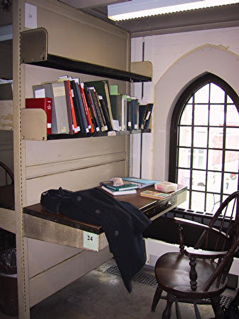 study carrel  - a little slot or niche in an age old library. a stack of books from its regular occupant. a coat thrown over bruqusely, an ornate chair in an older style.