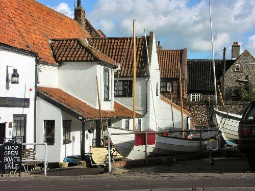 Wells, Norfolk 'Boats for Sale' - Wells-next-the-Sea is one of the most attractive towns on the North Norfolk Coast.  From the long sweeping beach bordered by pine woodland, along the gentle harbour with small fishing boats and children fishing for crabs, past the shops on Staithe Street with not a chain store in sight, to the tree-lined park with its fine Georgian houses, quiet pubs and restaurants - Wells is an unspoiled seaside destination, waiting to be discovered.  This shows the backs of some of the cottages, one of which is a chandlers which also sells boats.