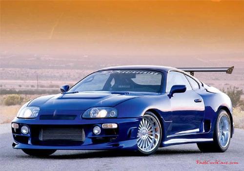 1998 Toyota Supra - Blue 1998 Toyota Supra with wide body kit, silver rims, and aluminum wing from front driver's side angle on road