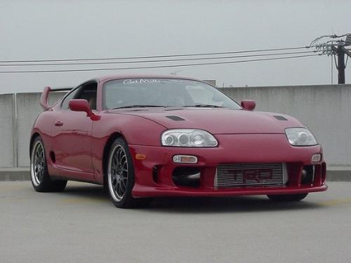 1998 Toyota Supra - Red 1998 Toyota Supra with gunmetal rims and Evo spoiler from front passenger side parked on roof of parking garage