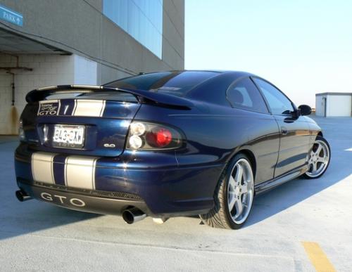 2005 Pontiac GTO - Blue 2005 Pontiac GTO with silver racing stripes, silver Axis rims, and black tails from rear passenger's side parked on roof in parking garage