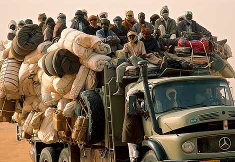 passengers - 'The trucks—big green flatbed diesels—are loaded to preposterous heights. Boxy steel shipping containers provide the sturdy foundation for huge burlap sacks containing prayer mats, sandals, blankets…and woven plastic bags labeled 'China Rice/Product of Libya.' Then—often 15 to 20 feet (4 to 6 meters) off the ground—rides an upper layer of passengers draped in robes and packed together as tight as the rice in the white sacks they sit upon.'