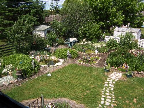 Wide view of our Au Natural Country Garden - This picture is a wider shot of your Au Natural garden. The picture may look slightly grainy...because it was taken in the screened inner upper deck 'gazebo.' It does give a good overall view of one sie of the garden. Our yard is landscaped on both sides and along the back with a circlular brick herb wheel in the middel of the back path.