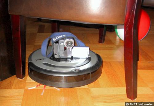 iRobot's new 'robust' Roomba - In addition to vacuuming both floors and carpets without sucking in rug fringe, the new generation of robots can sense when to slow down around furniture and walls.   'The robot sends out a beam of infrared light and when the light gets bounced back to the robot it says, 'OK, I'm near a wall. I should slow down a bit before I hit this wall,'' Preneta said.  The Roomba, apparently, is also robust enough to carry around a camera while it vacuums, as a CNET News.com senior reporter making a Roomba's-eye-view video demonstrates in this photo.