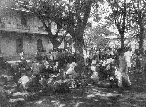 Fruit Vendors - The Philippines old Cavite fruit market. 'This photograph represents the native fruits, melons, etc., usually found in the markets of the various cities and towns. The stands are generally kept by women amd girls, all of whom smoke cigars and cigarettes.'