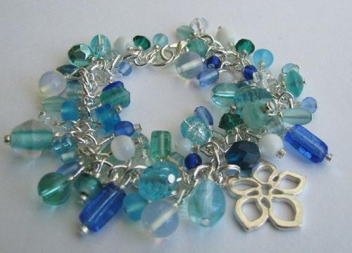 Tropical Blues Bracelet - This 7 1/2' bracelet is overflowing with various size & shapes glass beads in blue, aqua and white. Moonstone beads were added as they reflect the beautiful blues in this creation. Finishing this bracelet is a brushed silver hibiscus flower charm. Available in my Etsy.com shop
