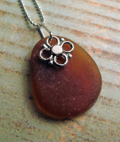 Brown Sea Glass Necklace - A beuatifully smooth and rounded piece of chocolate beach glass, measuring 7/8' in length, hangs from a 18' sterling silver chain. The beach glass gem is accented with a small silver flower charm.
