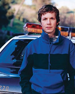 Beck - Beck wearing a blue windbreaker posed in front of a cop car