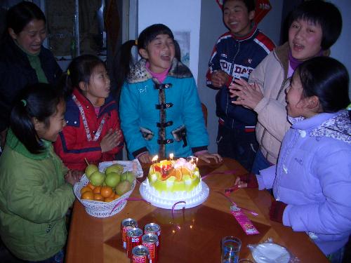 birthday cake and party - this is a photo of the kids of my friends, who come together to celebrate the girl's tenth birthday, the girl in blue. they are singing 'happy birthday to you'.