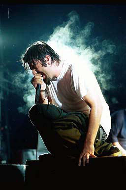 Chino from Deftones - A picture of Chino from the band Deftones. Screaming in the mic on stage with fog and lights behind him.