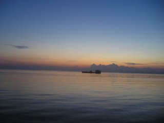 Dumaguete at Sunrise - This is a view of the Island of Siquijor from across the Boulevard in Dumaguete City, in Negros Oriental province. Taken early in the morning as the sun is just rising, the solitary boat sits on calm waters while colors of the morning sun diffuses all around it.