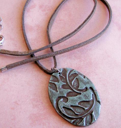 Moss on Brown Leaf Print Pendant/Necklace - 1 1/2' x 1' oval. Brown polymer clay, stamp with a pretty leaf print, then dry-brush painted w/ a mossy green acrylic paint and coated with a gloss glaze for protection. This earthy pendant hangs on an 18' adjustable brown suede-like cord necklace.