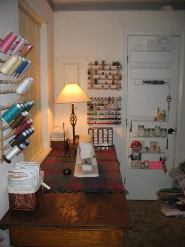 my sewing area - Here is a pic of my sewing area at my apt, one of my sewing machines is sitting on an antique writing desk my mom gave me from a bank. It is solid oak and the measurements are 3ft x 6ft with decorated legs, with 2 drawers in the front for misc sewing supplies and my manuals.   Since this pic was taken I have added a newer sewing machine and a serger. On the walls are spool holders. Some of my spools are antiques that I bought and some that were given to me.