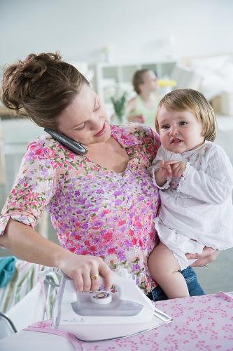 Mom gets Help - Here is a picture of a mother who is ironing. She is holding a child on her arm too. This can be called multitasking.