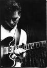 Playing the guitar - Theres a picture of a guy playing his guitar. His guitar is electric. The back round is black.