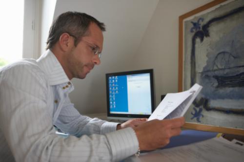 man working at home - man sitting at a desk holding documents working at home