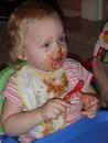 so precious - Picture of a caucasian infant baby sitting at a blue table with a bib on her face covered in food and all over her bib