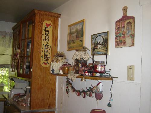 Kitchen Wall - Here is a picture of a wall in my kitchen, showing some of the things that are hanging on my wall, such as the cutting board with the painting on it, the pictures with farm scenes, the shelf with candles and country decorations on it.