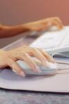 getting the job done - A picture of two caucasian hands at a desk, with one hand on a mouse and the other one on the left side of the white keyboard
