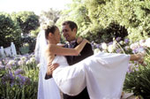 Romance in the air! - Portrait of a newlywed groom carrying his bride down a gravel path.