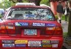 My car does not look like this, yet at least - Picture of the back of a small red car showing a bunch of bumper stickers
