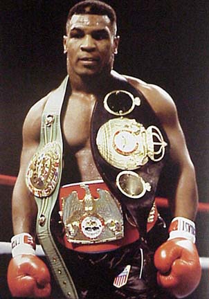 Mike Tyson And The Gold - Mike Tyson wearing his boxing gear standing in a boxing ring with a gold belt around his neck and a gold eagle around his waist.