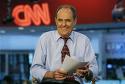 Jack Cafferty from The Cafferty Files, CNN - Picture of Jack Caffert of the Cafferty Files on CNN holding papers in his hand at his tv desk with a laughing smile with big neon CNN sign in the background