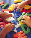 education - kids playing with letters on a table. The letters are all over the table and there are heaps of them, you can only see the kids hands and there are lots and lots of hands all trying to put the letter togther.
