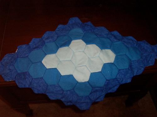 Blue Diamond Centerpiece Mat - This centerpiece mat is based on a variation of the grandmother's flower garden pattern. Rather than a circular shape that looks like a flower, this is extended on each end to create a diamond. It is completely hand sewn. Now on sale in my Etsy shop.