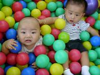 a fat boy and a thin one - a fat boy and a thin one are playing in a children's park.they are lying in a bed which is filled with colorful balls.