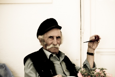 Man Smoking Pipe - An old man smoking a pipe in Mykonos, Greece. The men has gray mustaches and old hand watch which he got from his father many years ago. This photo has nice aura.