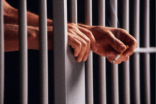 Locked up in a prison - Man locked up in a prison smokes a cigarette.