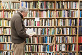 Books - Man reading a book from a large bookshelf