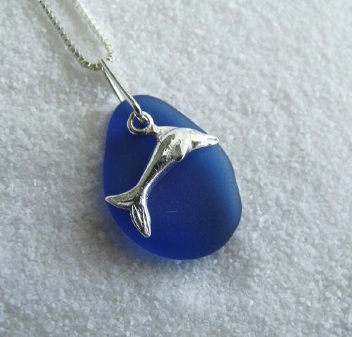 Leaping Dolphin Cobalt Blue Sea Glass Necklace - A sterling silver dolphin charm accented by cobalt blue sea glass gives the impression of a dolphin leaping out of the ocean. The pendant dangles from a sterling silver necklace.