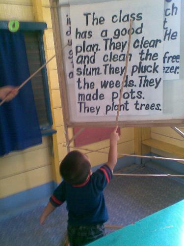 a young student - a picture of a very young boy, about 3 years old, holding a stick while reading the words on the visual aids.