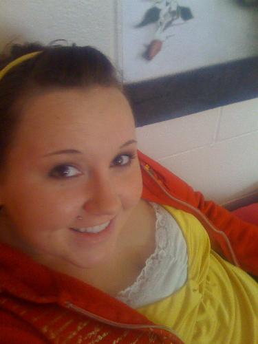 It's me smiling next to my poster - It's me in a red jacket and yellow shirt sitting on my bed in my dorm next to my poster.