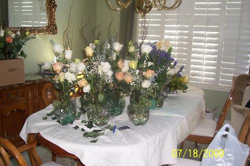 Floral Arraignments  - Wedding reception table centerpieces made of fresh roses in assorted colors and branches arraigned in glass vases with iridescent glass stones in the bottom of the vase for added color.