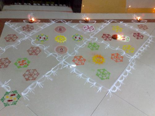 Diwali Rangoli - Rangoli, also known as Alpana, Kolam and by other names is a traditional art of decorating courtyards and walls of Indian houses, places of worship and sometimes eating places as well. The powder of white stone, lime, rice flour and other paste is used to draw intricate and ritual designs.   Although Rangoli art is Maharashtrian in origin, it has become quite popular all over the country. Each state of India has its own way of painting Rangoli. One characteristic of Rangolis is that it is painted by commoners. On some special occasions like Dipavali it is painted in every home, with or without formal training in Rangoli art. The art is typically transferred from generation to generation and from friend to friend.   Traditionally Rangolis are painted or created out of colored sand/rice powder. A symmetrical pattern or picture of Gods, Goddess, Dancers, Diyas etc. is drawn and colored rice powder/sand is then layered on top to form a picture. A symmetrical rangoli pattern can be drawn on paper or card and then decorated by children with crumpled tissue paper.   Spaces can be created within the rangoli design to place diyas. One can also use flower petals of different colors such as golden marigolds, bright red roses to add that extra dimension to the pattern. With a little bit of imagination, a dash of aesthetic sense and dollops of patience, one can create a piece of art with colors.   Most of the patterns are circular indicative of the endlessness of time. The day-to-day Rangoli patterns are simple or intricate. The most common rangoli designs start with dots which are connected to form lines and other geometrical shapes such as swastika, aum, stars, squares, circles, triangles etc. These geometrical patterns must be formed in a continuous, unbroken lines.