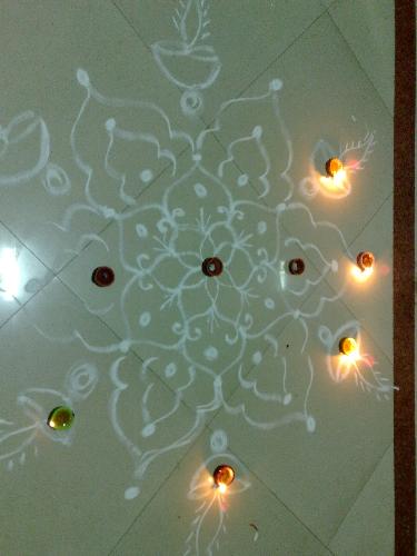 Diwali Rangoli - Rangoli, also known as Alpana, Kolam and by other names is a traditional art of decorating courtyards and walls of Indian houses, places of worship and sometimes eating places as well. The powder of white stone, lime, rice flour and other paste is used to draw intricate and ritual designs.   Although Rangoli art is Maharashtrian in origin, it has become quite popular all over the country. Each state of India has its own way of painting Rangoli. One characteristic of Rangolis is that it is painted by commoners. On some special occasions like Dipavali it is painted in every home, with or without formal training in Rangoli art. The art is typically transferred from generation to generation and from friend to friend.   Traditionally Rangolis are painted or created out of colored sand/rice powder. A symmetrical pattern or picture of Gods, Goddess, Dancers, Diyas etc. is drawn and colored rice powder/sand is then layered on top to form a picture. A symmetrical rangoli pattern can be drawn on paper or card and then decorated by children with crumpled tissue paper.   Spaces can be created within the rangoli design to place diyas. One can also use flower petals of different colors such as golden marigolds, bright red roses to add that extra dimension to the pattern. With a little bit of imagination, a dash of aesthetic sense and dollops of patience, one can create a piece of art with colors.   Most of the patterns are circular indicative of the endlessness of time. The day-to-day Rangoli patterns are simple or intricate. The most common rangoli designs start with dots which are connected to form lines and other geometrical shapes such as swastika, aum, stars, squares, circles, triangles etc. These geometrical patterns must be formed in a continuous, unbroken lines.